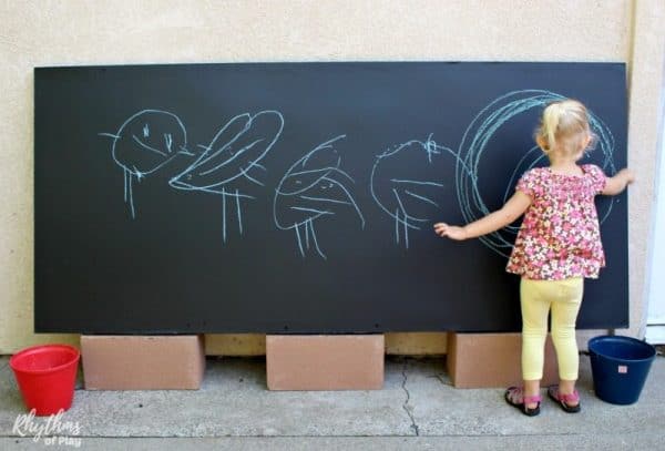 Preschooler drawing on a DIY outdoor chalkboard (photo of Charlize Kartychok by Nell Regan K. founder of Rhythms of Play)