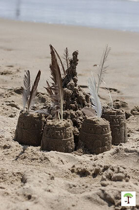 Sand castle with sand towers all around it decorated with feathers and other natural materials.