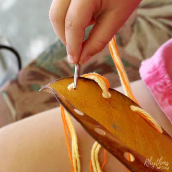 Child sewing a DIY fall leaf lacing cards with darning needle and yarn. 