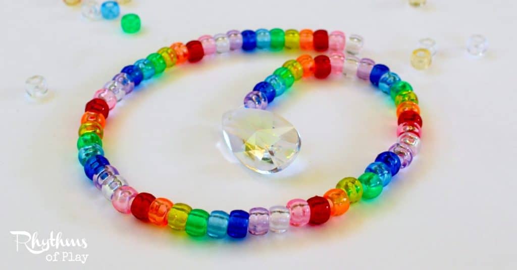 Making a pony bead and prism suncatcher is a fun fine motor activity for kids and adults of all ages. Suncatchers made out of beads in a rainbow of colors are lovely home decor to hang in a window and enjoy. The prism will cast beautiful rainbows all over the room when the sun hits it. These would make a great decoration or favor idea for a rainbow party. This DIY craft project also makes a wonderful gift idea for Christmas, birthdays or any other occasion!