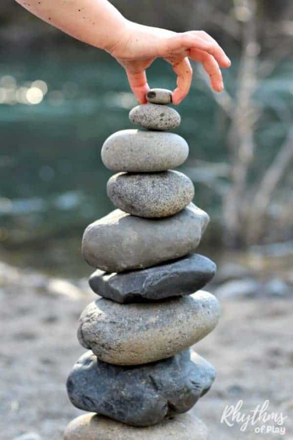 Child balancing a rock on top of a stone stack to create nature land art. 