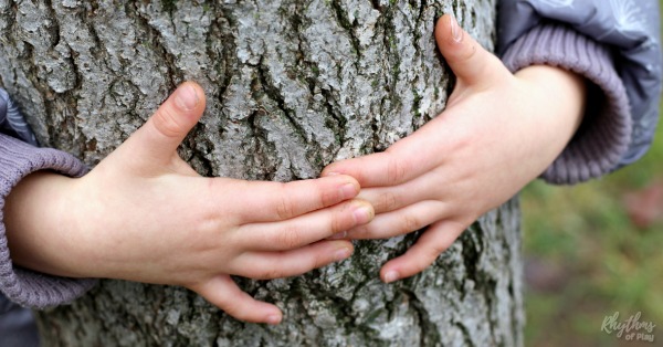 Young child's hands hugging a tree outside in nature.