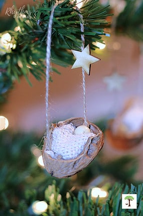 DIY Baby Jesus Christmas ornament craft in a half-walnut shell hanging on a Christmas tree.