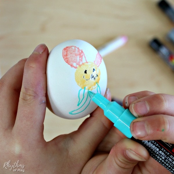 child drawing an Easter Bunny on an egg with a paint pen (painted egg craft by Charlize Kartychok)