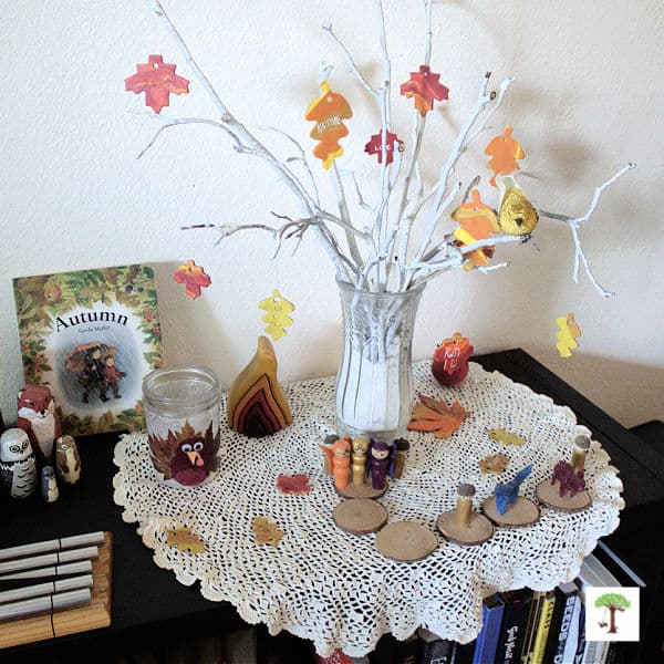 autumn or fall-themed nature table idea with a thankful tree, turkey leaf lantern, fall fairy peg doll toys, Autumn board book, etc.