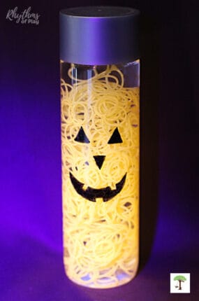 DIY Halloween sensory bottle with a friendly pumpkin jack o' lantern face and glow in the dark orange loom bands