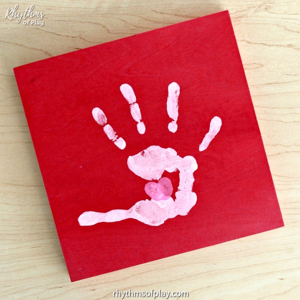"Kissing hand" handprint art craft with a thumbprint heart on a red wooden canvas (keepsake craft and photo by C. Kartychok and Nell Regan K. founders of Rhythms of Play)