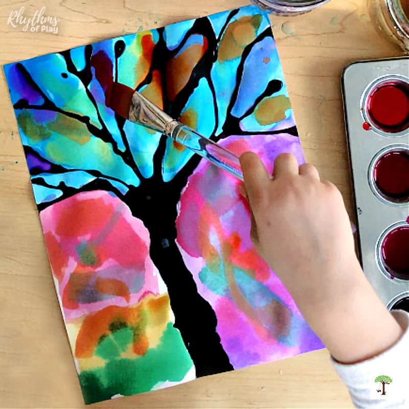 Child painting winter tree silhouette art using watercolors and a flat watercolor paintbrush