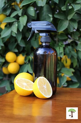 Homemade wood cleaner and polish in amber bottle sitting on polished wooden surface with lemons.