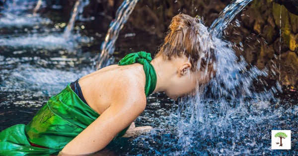 Celtic woman in green dress dipping her head underwater to purify and cleanse herself on Imbolc.