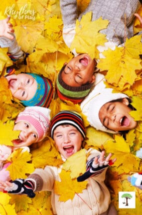 Kids celebrating fall atumnal equinox smiling in a pile of fall leaves.