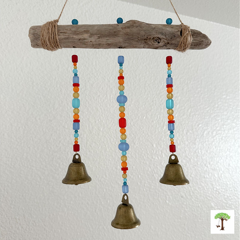 Three-strand sea glass DIY wind chime hanging from driftwood with bronze bells for the pendant at the end of each beaded strand.