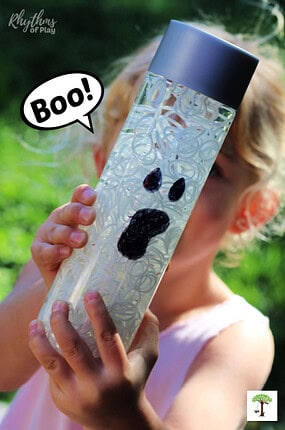 Kid holding DIY Halloween Sensory Bottle that looks like a ghost with "Boo" speech bubble.