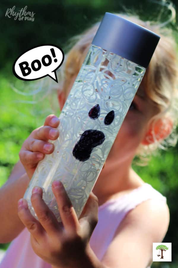 Kid holding DIY Halloween Sensory Bottle that looks like a ghost with "Boo" speech bubble.