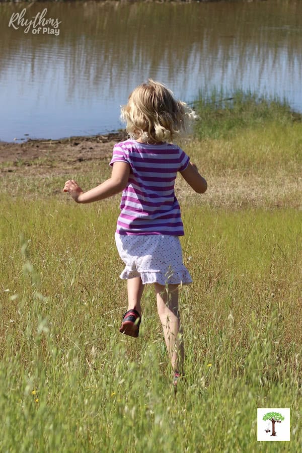 Young girl running through tall grass beside a pond enjoying playtime in nature.